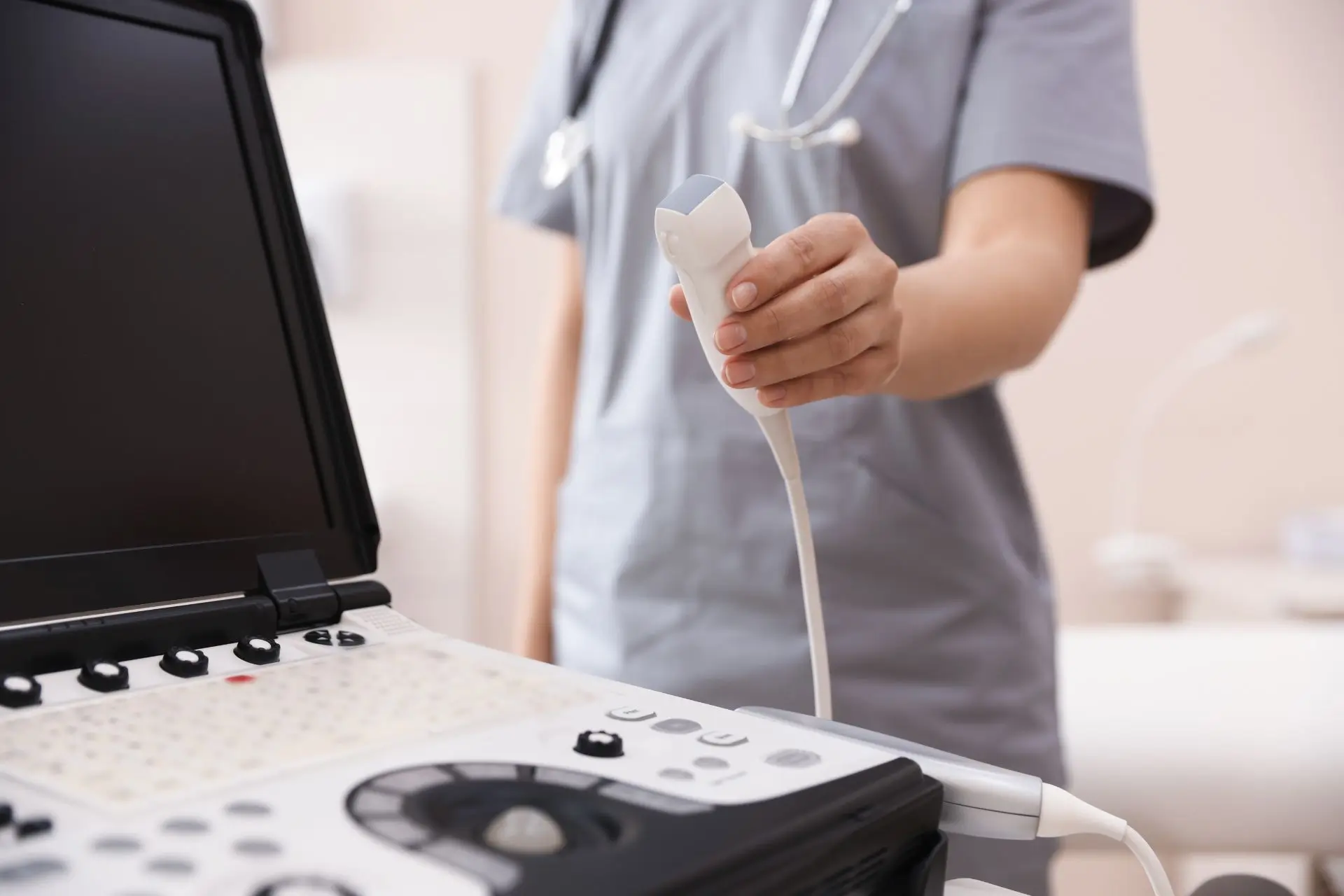 Sonde eines Sonographie-Geräts in Nahaufnahme mit der Hand einer Frau, welche einen Arztkittel trägt