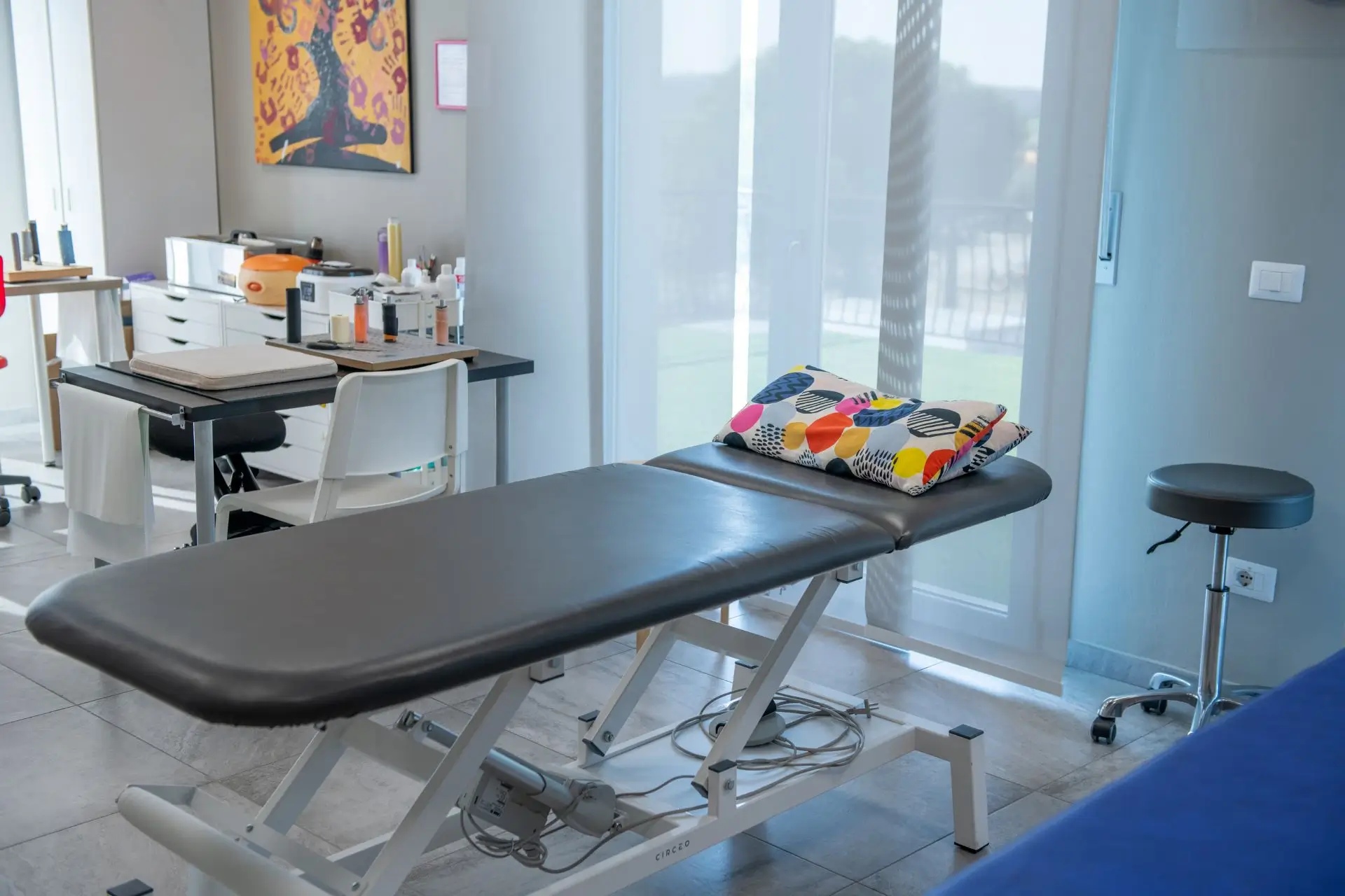 Heller Raum in dem eine hydraulisch verstellbare Therapieliege steht, daneben ein Arztsessel